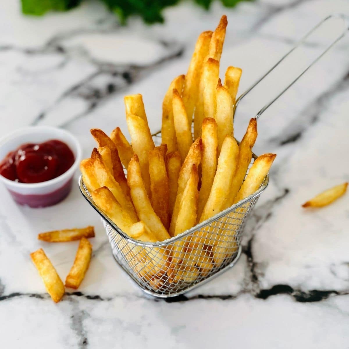 A mesh fry basket filled with golden brown, crispy air fryer frozen french fries.