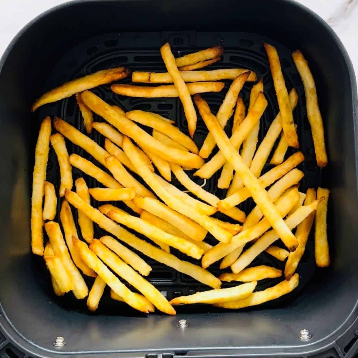 The golden brown and crispy french fries in the air fryer basket at the end of the cooking time.