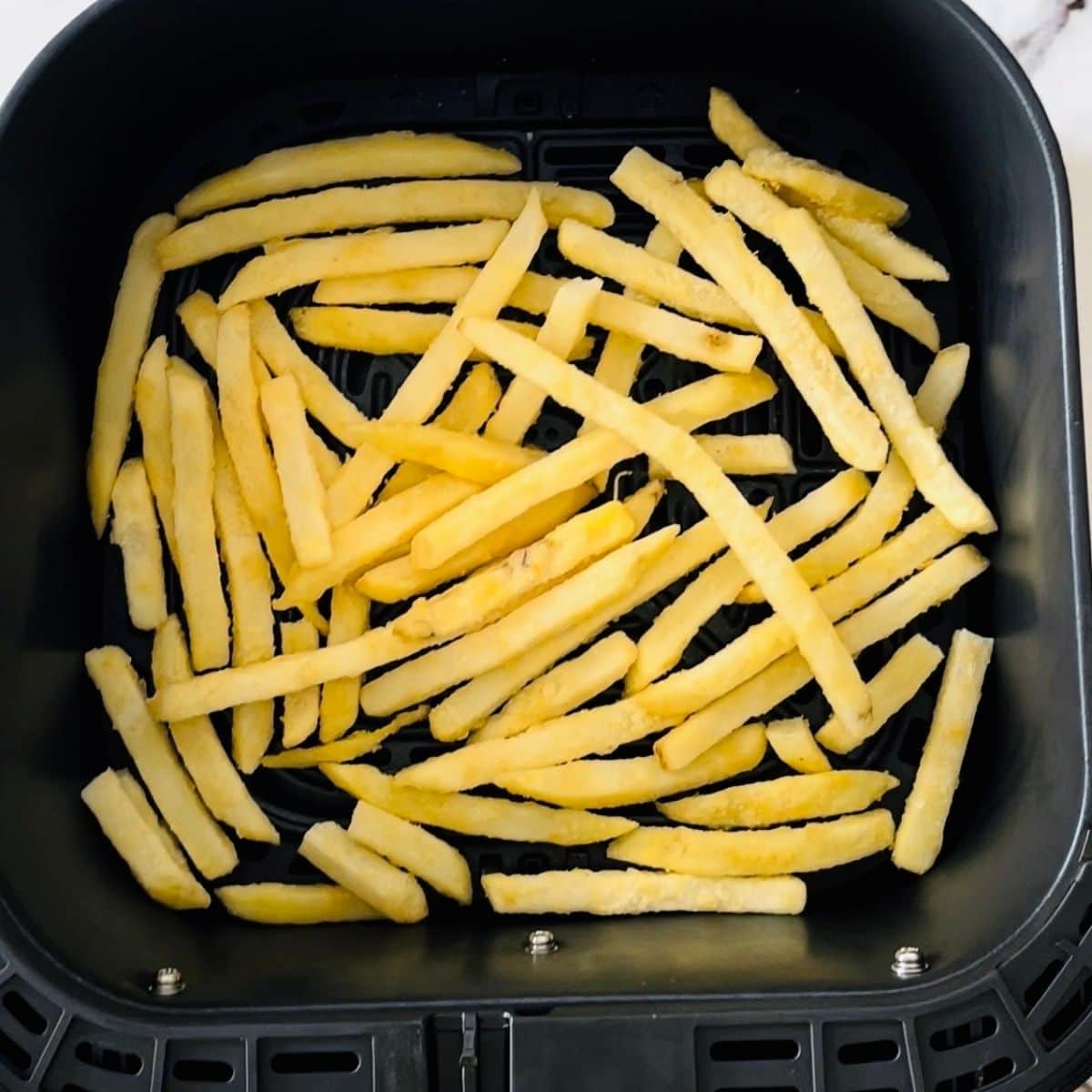 Frozen fries in the air fryer basket in an even layer.