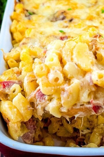 Spoon lifting creamy baked brisket mac and cheese from a casserole dish.