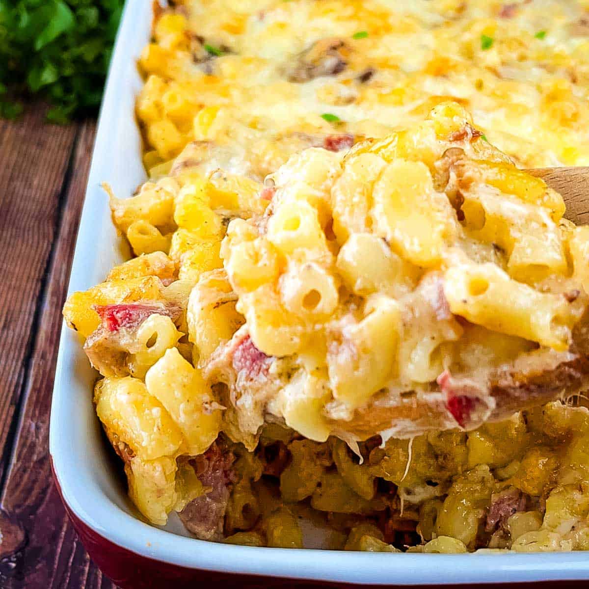Spoon lifting creamy baked brisket mac and cheese from a casserole dish.