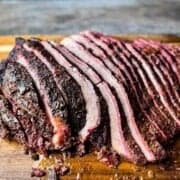 Sliced hot and fast smoked brisket with a dark bark and visible smoke ring resting on a wooden cutting board.
