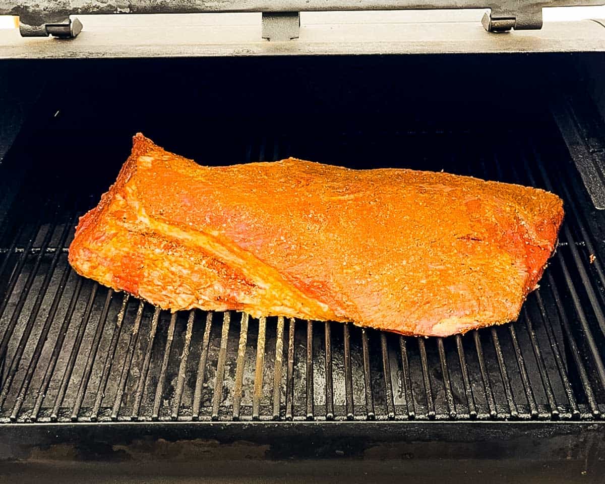 The seasoned brisket directly on the smoker grates of a pellet grill.