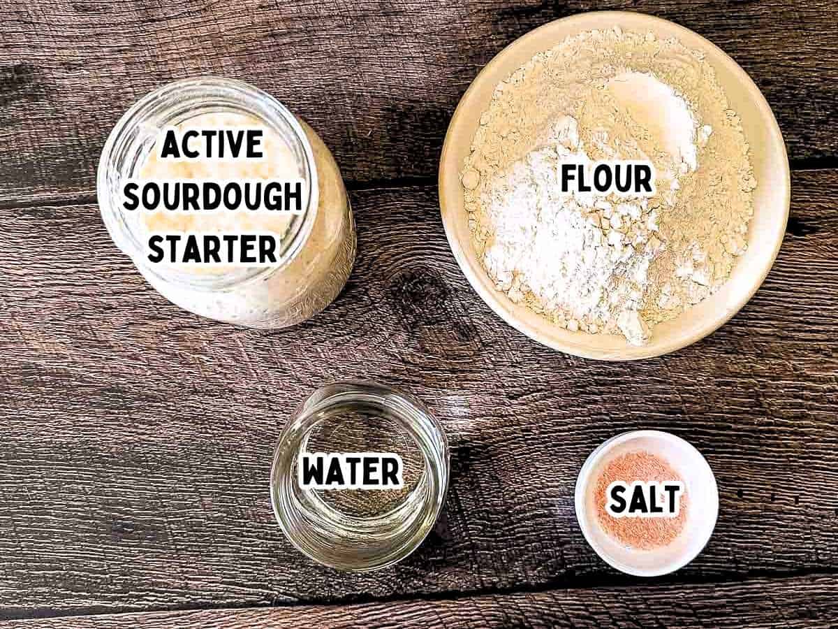 Labeled ingredients for no knead sourdough sandwich bread in bowls on a wooden table.