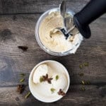 Ninja Creami chai ice cream being scooped from a pint container topped with star anise and green cardamom pods.