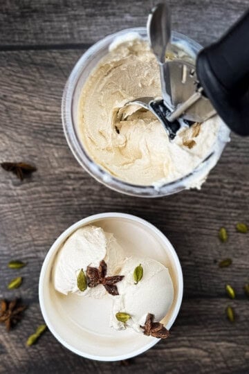 Ninja Creami chai ice cream being scooped from a pint container topped with star anise and green cardamom pods.