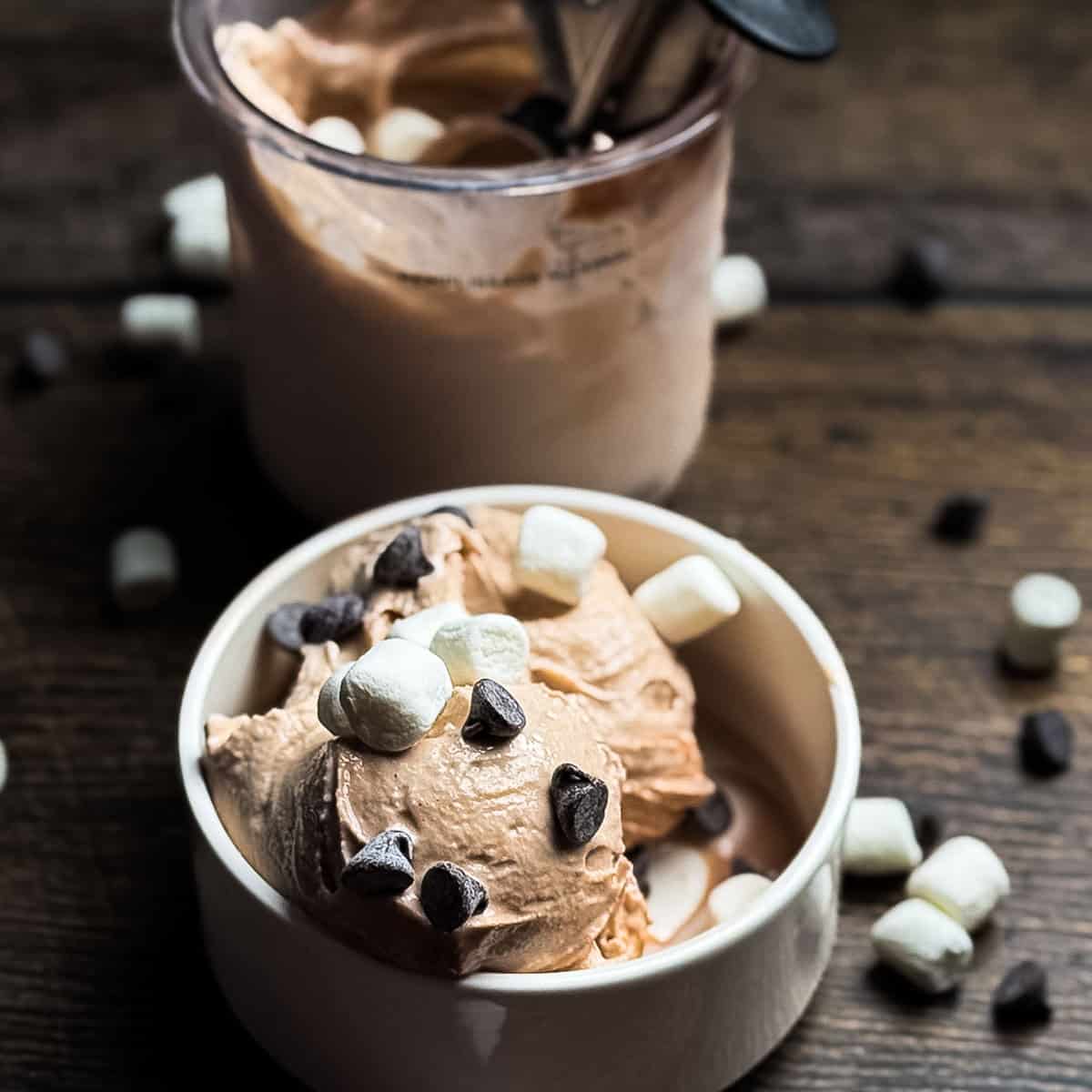 Ninja Creami hot chocolate ice cream topped with mini marshmallows and chocolate chips in a white bowl.