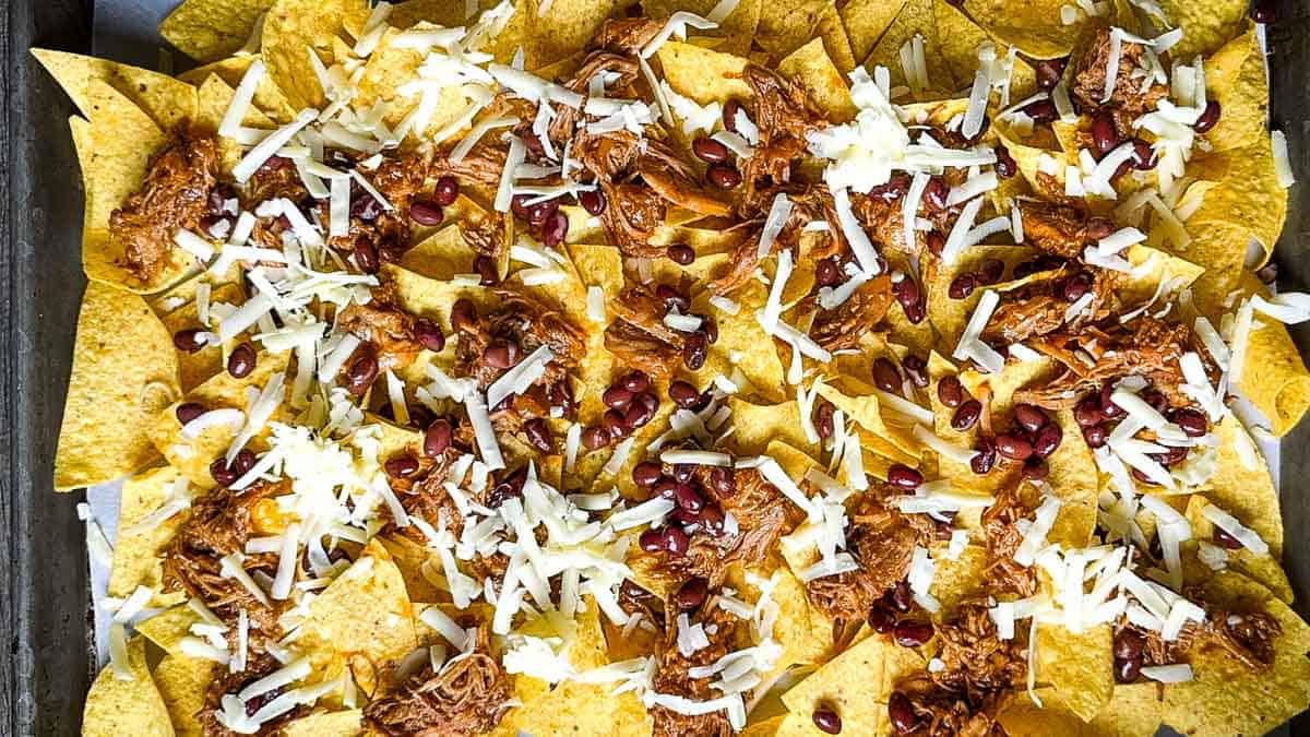 Shredded cheese sprinkled over pulled pork and black beans on tortilla chips.