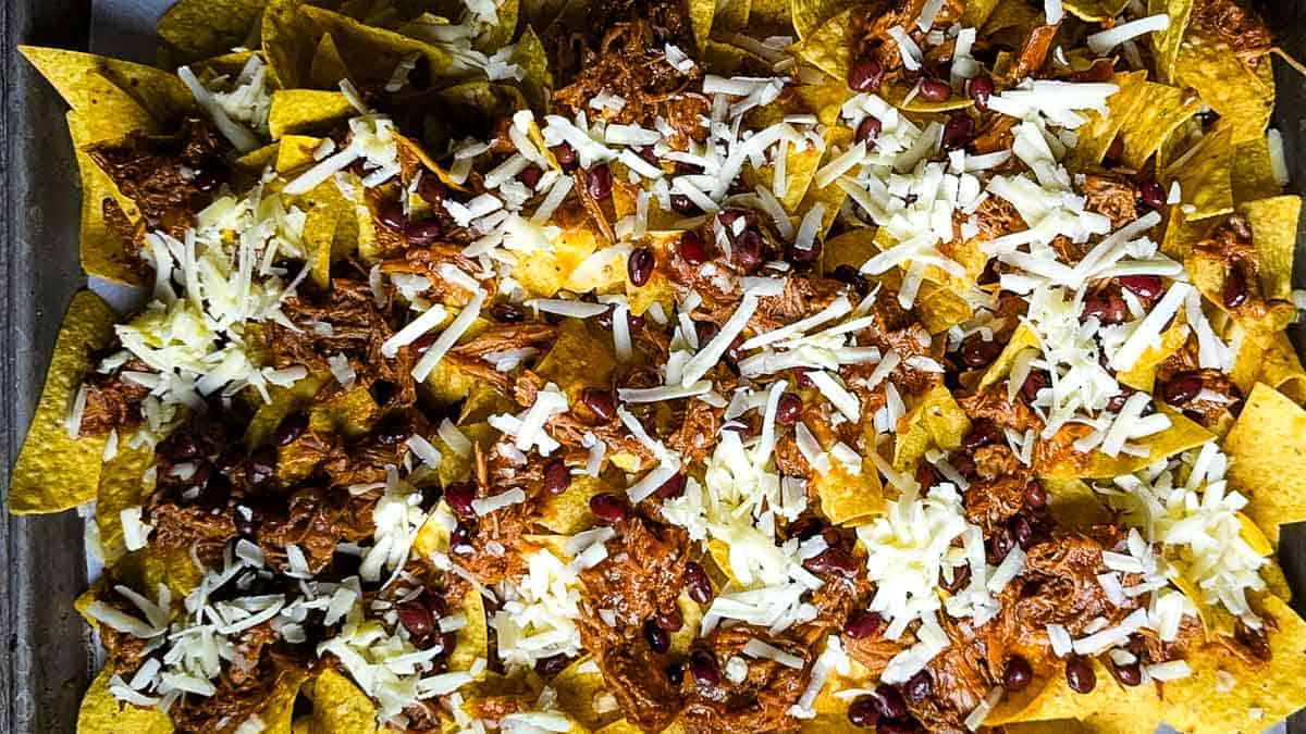 Assembled pulled pork nachos ready to bake on a sheet pan.