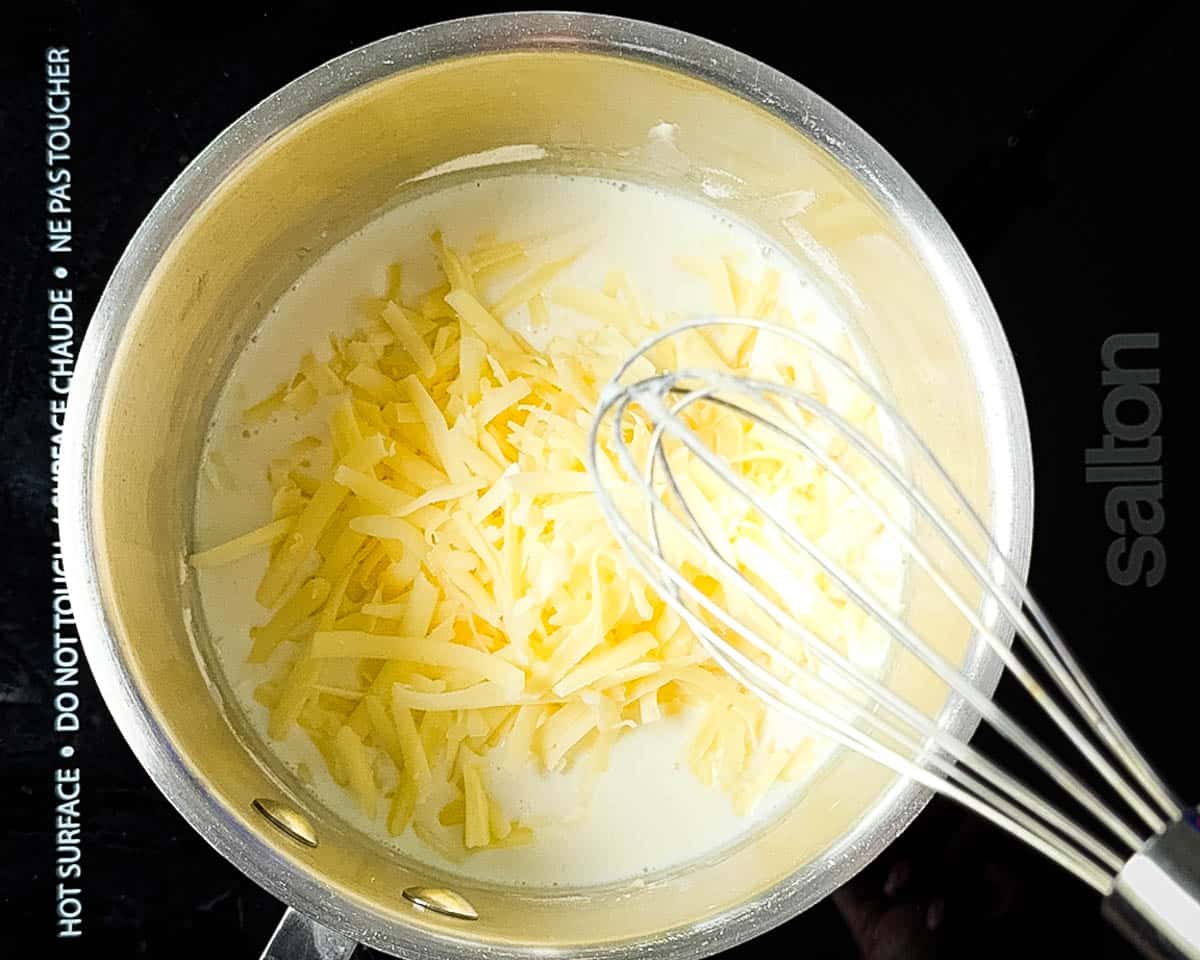 Creamy homemade cheese sauce being whisked smooth in a saucepan.