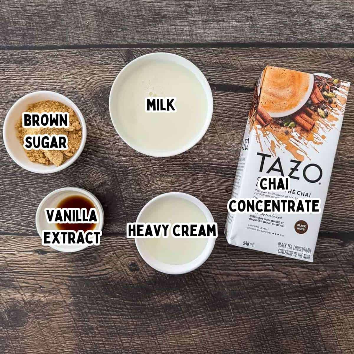 Labeled ingredients for Ninja Creami chai ice cream on a wooden table, including chai concentrate, milk, cream, brown sugar, and vanilla extract.