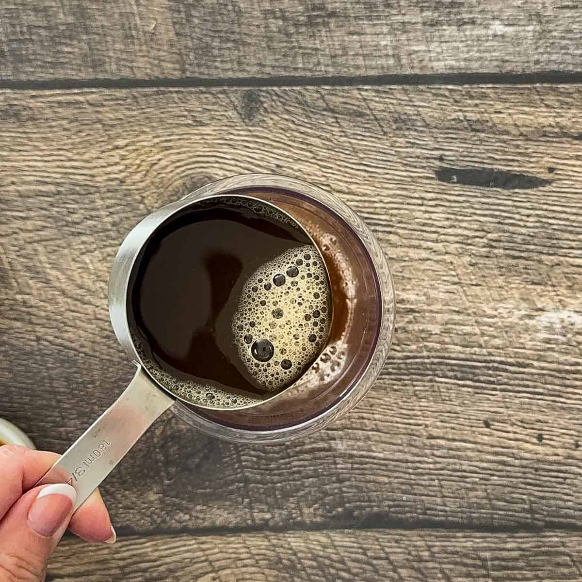 Pouring chai concentrate into Ninja Creami pint container to make ice cream base.