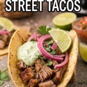 Slow cooker carnitas street tacos with tender shredded pork, crispy edges, pickled red onions, cilantro, avocado crema, and fresh lime on a warm corn tortilla.