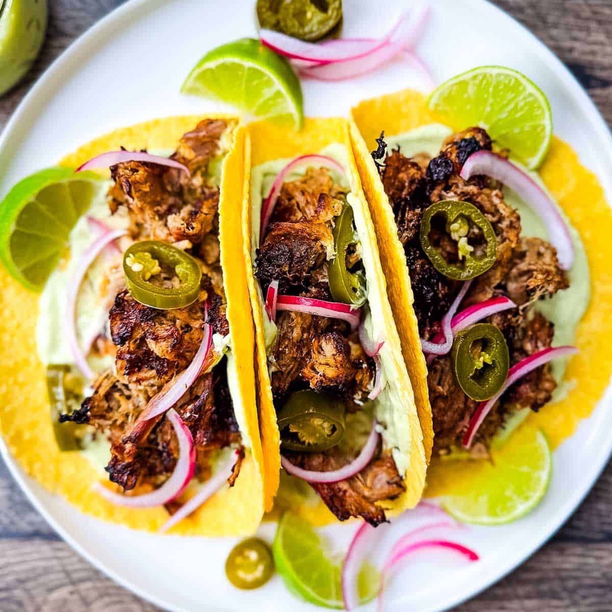 Carnitas street tacos with tender pulled pork, jalapeño slices, red onions, and avocado lime crema on corn tortillas.