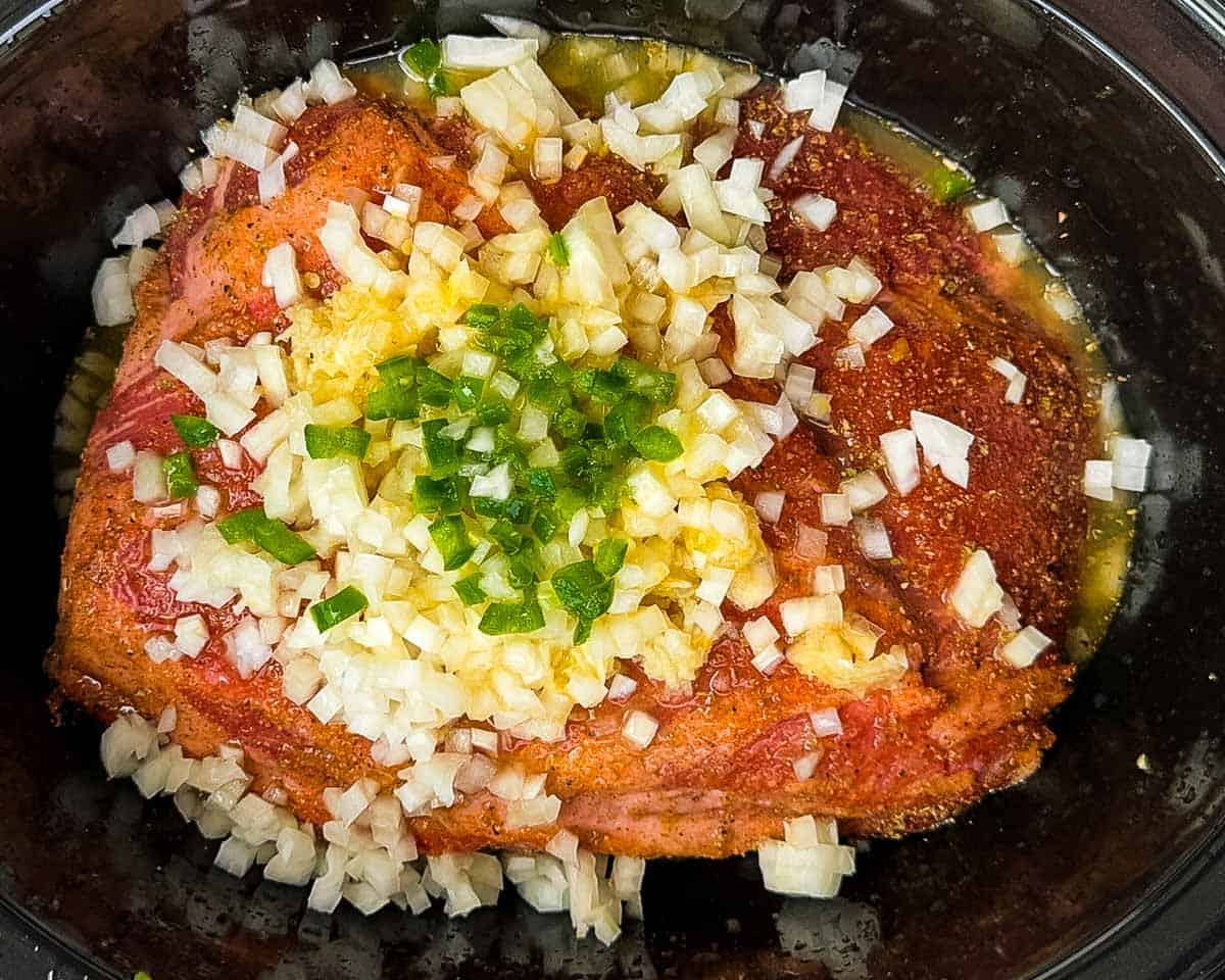 The seasoned pork shoulder in a slow cooker with the rest of the ingredients.