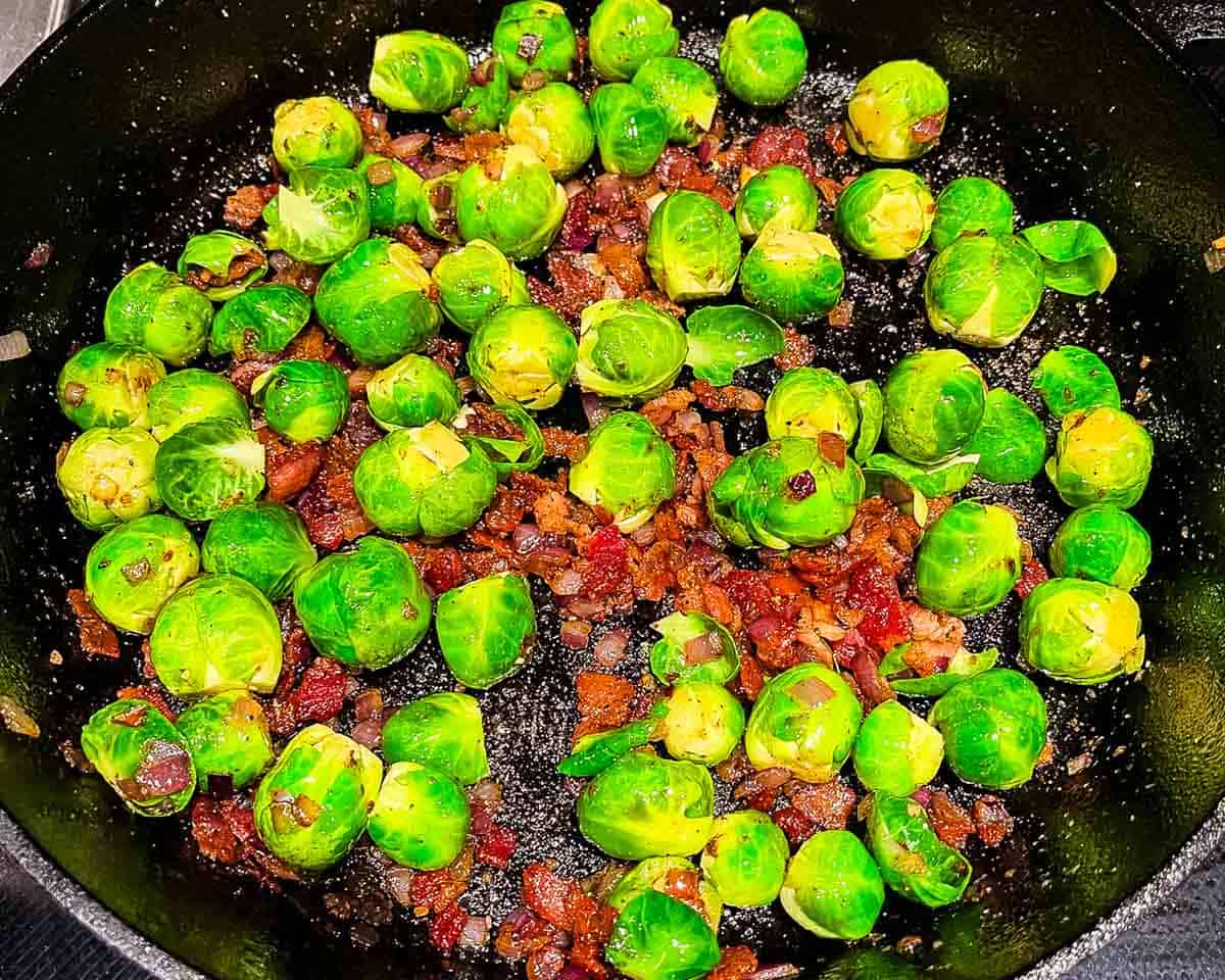 The Brussels sprouts, onion, and garlic combined in a cast iron skillet with bacon.