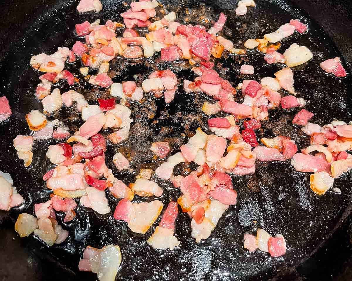Diced bacon cooking in a cast iron skillet.