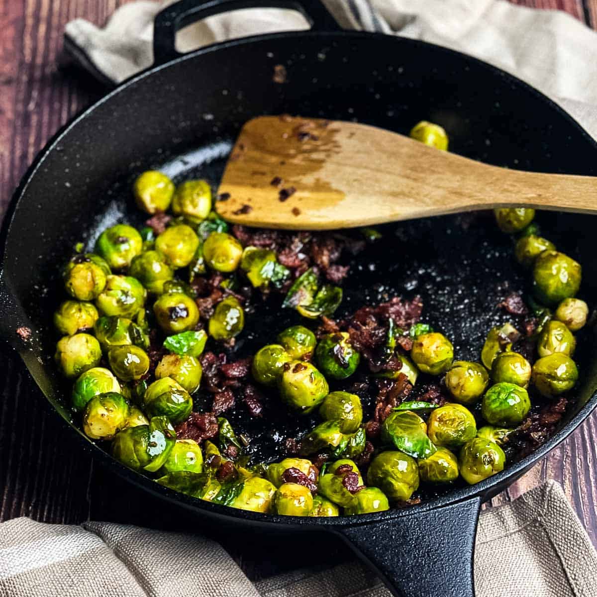 Smoked Brussels sprouts with bacon cooked in a cast iron skillet on a pellet grill.