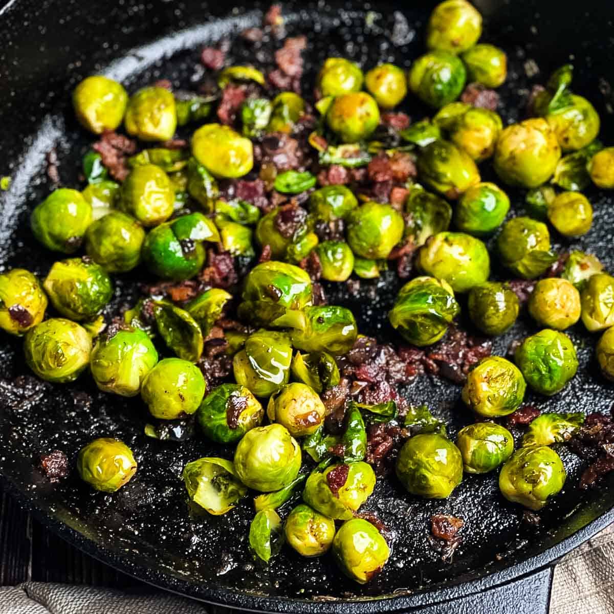 Brussels sprouts with bacon in a skillet showing crispy edges and crispy bacon.