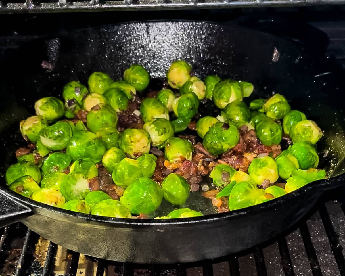 The Brussels sprouts in a skillet smoking in a pellet grill.