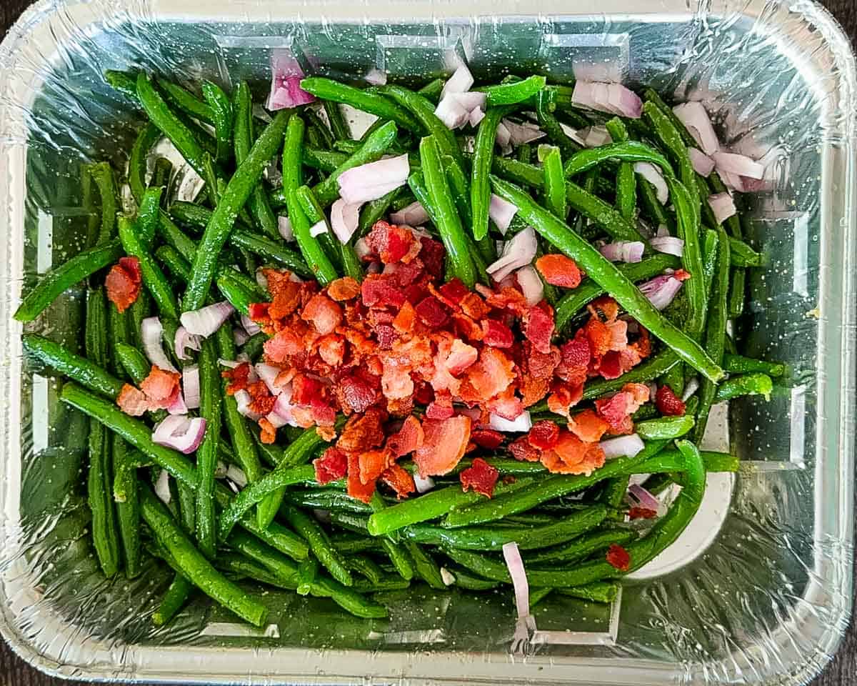 The bacon and red onion added to the foil pan.