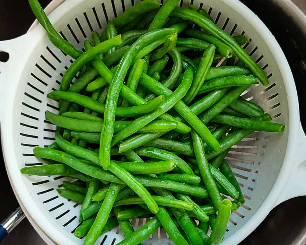 The blanched green beans being drained in a white colander.