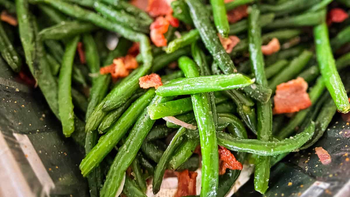 Juicy smoked green beans with bacon in a foil pan, ready to be served.