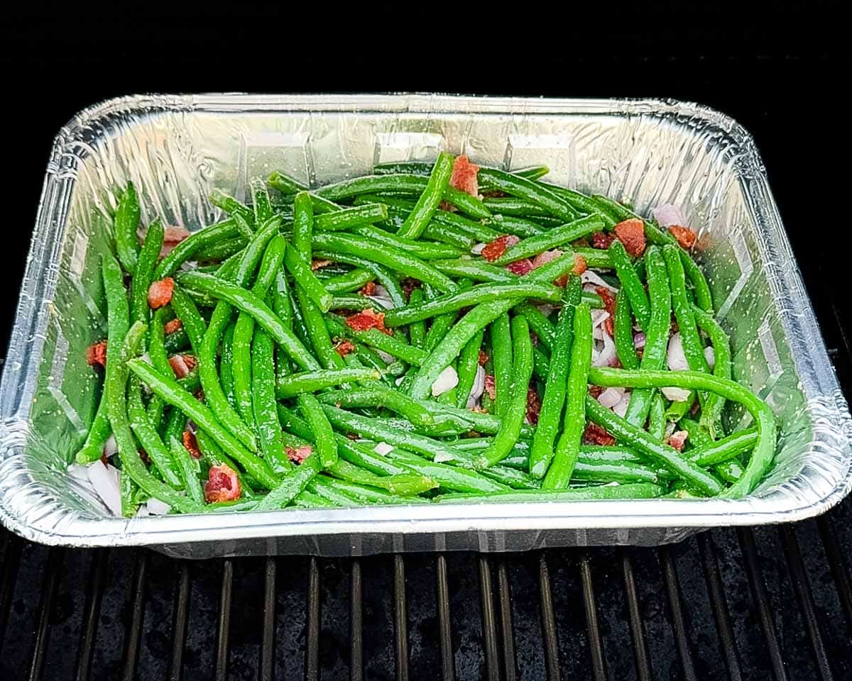The foil pan of green beans on the grill grates of a pellet grill.