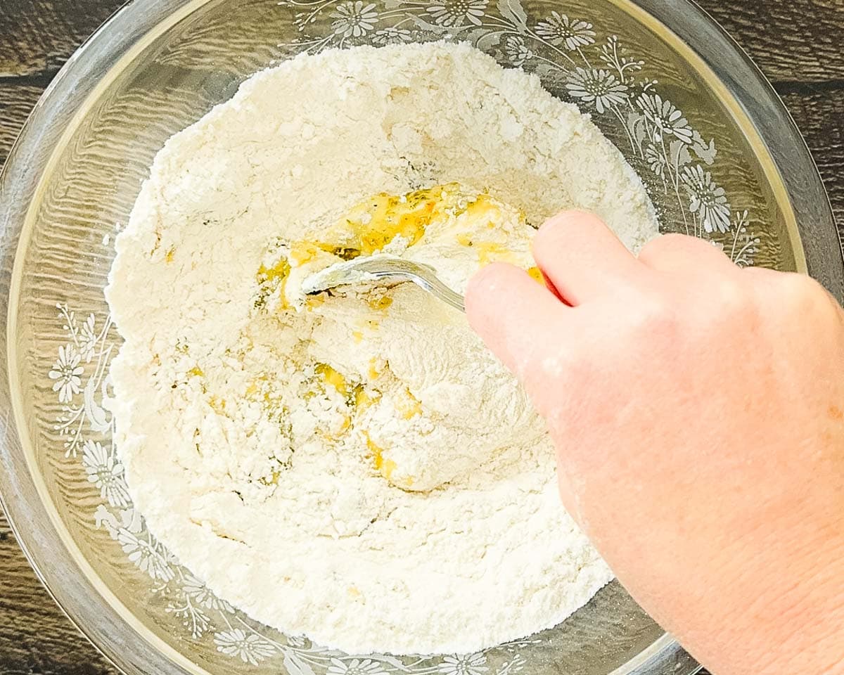 A hand using a spoon to combine the ingredients for the crackers in a large mixing bowl.