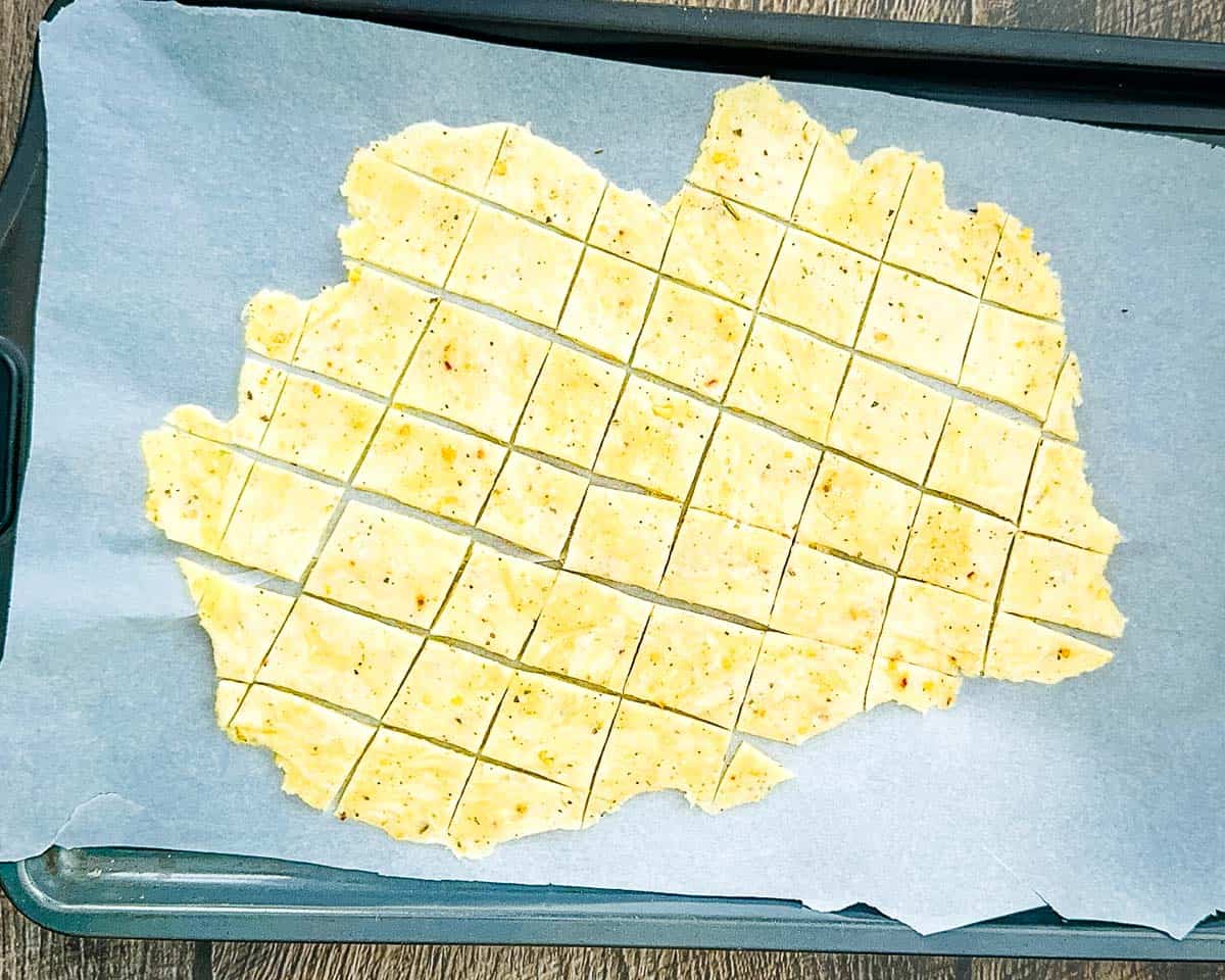 The dough on parchment paper rolled thin and cut into similar-sized squares, ready for baking.