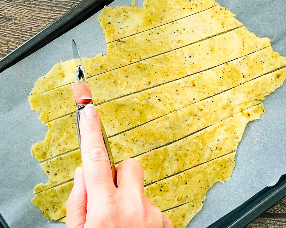 A hand using a pizza cutter to cut the rolled dough into squares.