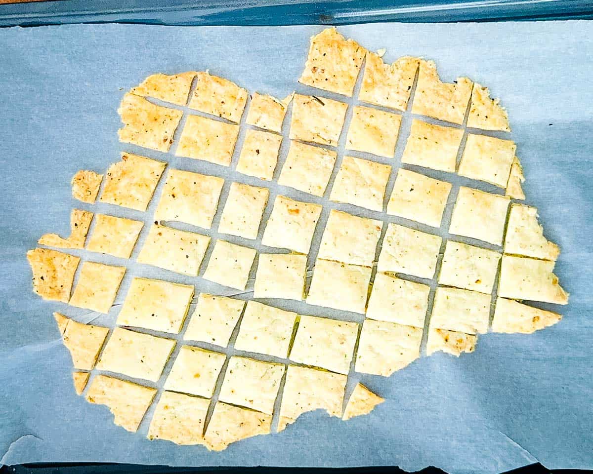 The baked sourdough discard crackers on a parchment paper-lined baking sheet, showing golden brown edges.