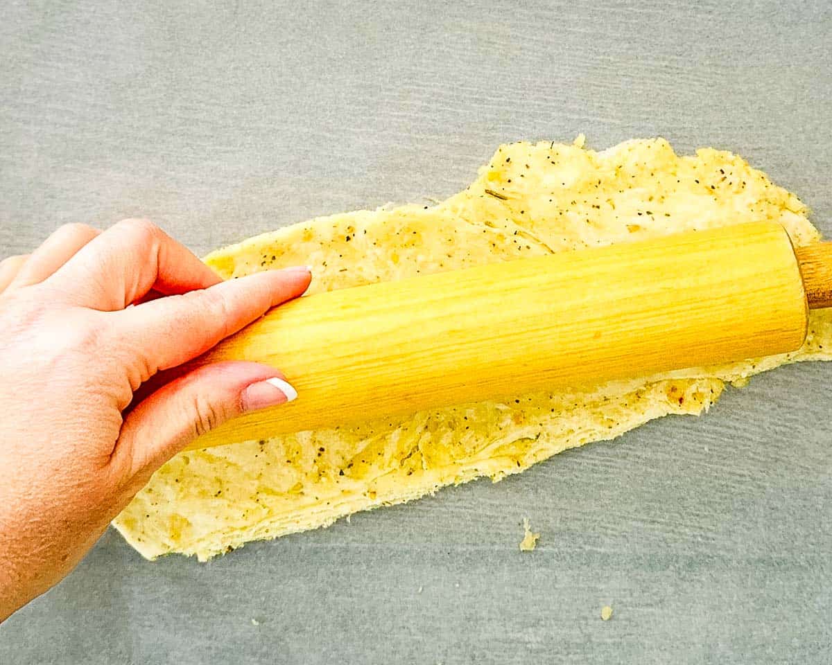 The dough being rolled out on parchment paper with a wooden rolling pin.