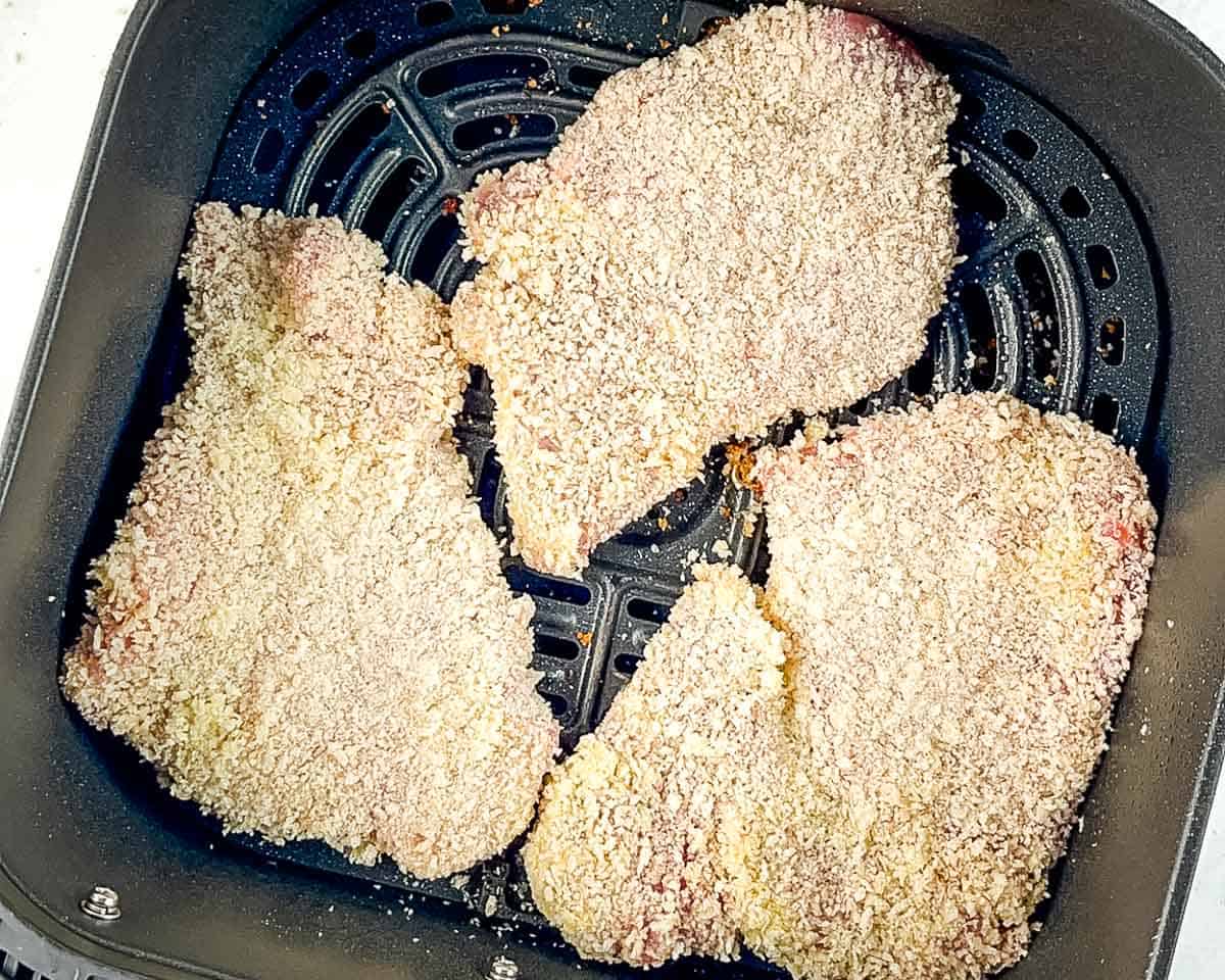 Breaded pork cutlets arranged in a single layer in the air fryer basket before cooking.