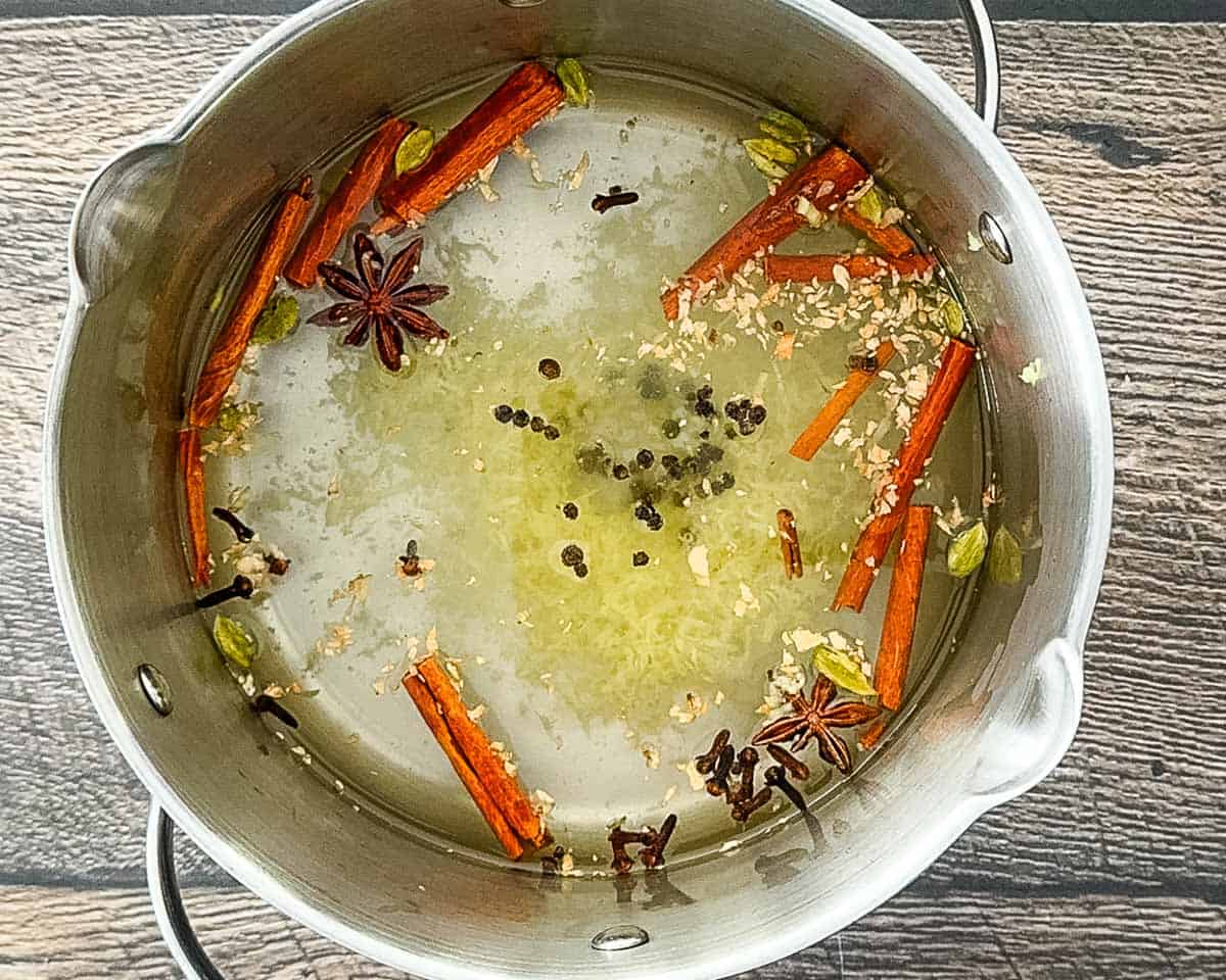 Simmering whole spices like cinnamon sticks, cardamom, and cloves in water in a saucepan.