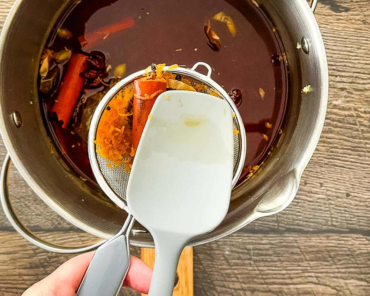 Pressing tea bags and spices through a fine mesh strainer to extract liquid.