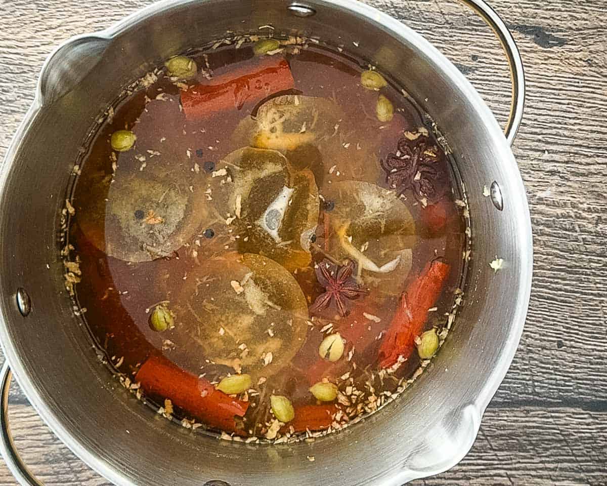 Tea bags steeping in spiced liquid in a saucepan after simmering.