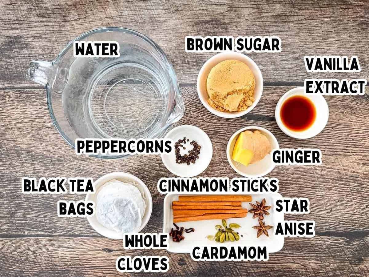 Ingredients for homemade chai tea concentrate including black tea bags, cinnamon sticks, cardamom, cloves, ginger, and brown sugar.