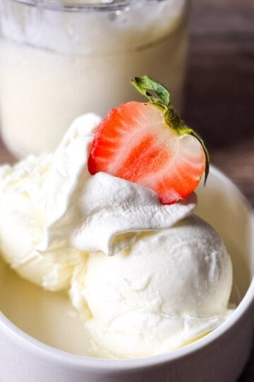 A white bowl filled with two scoops of creamy Ninja Creami frozen vanilla yogurt topped with whipped cream and a fresh strawberry slice.