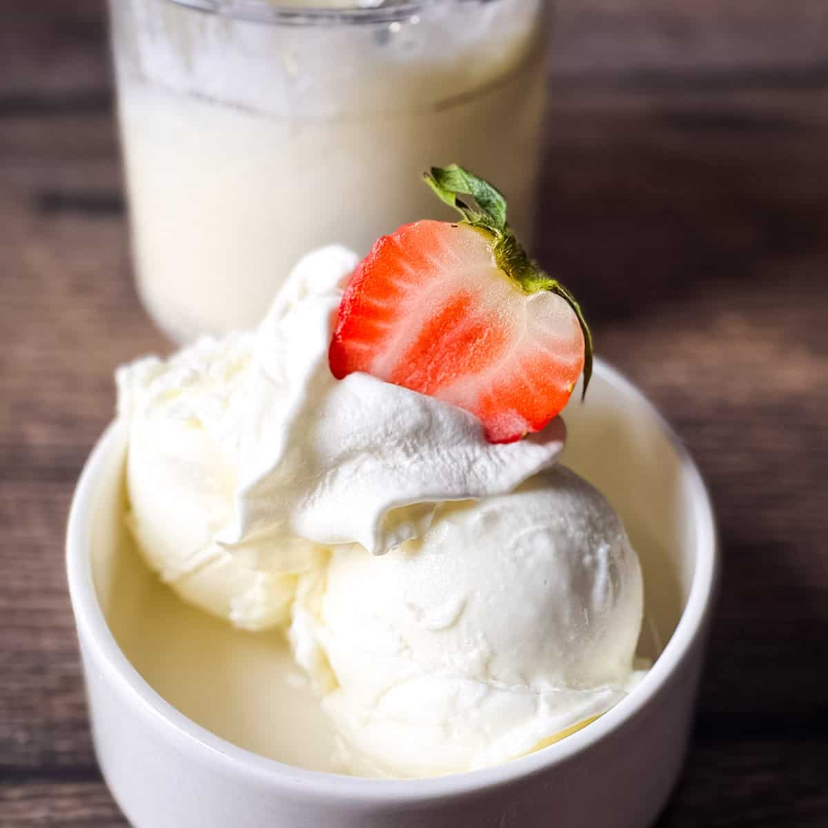 A white bowl filled with two scoops of creamy Ninja Creami frozen vanilla yogurt topped with whipped cream and a fresh strawberry slice.