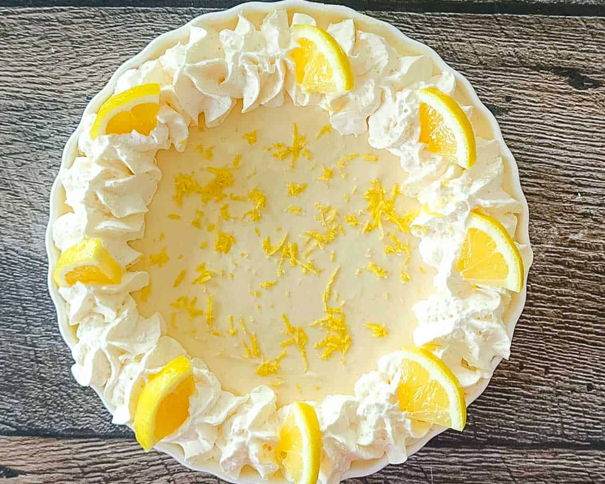 A No-Bake Lemon Cream Pie topped with whipped cream, lemon slices, and lemon zest.