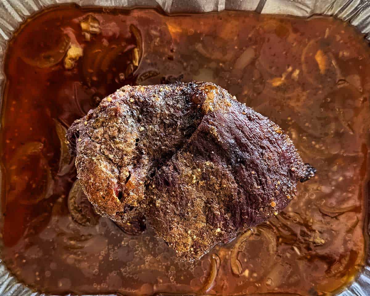 Smoked roast resting in rich braising liquid after resting.