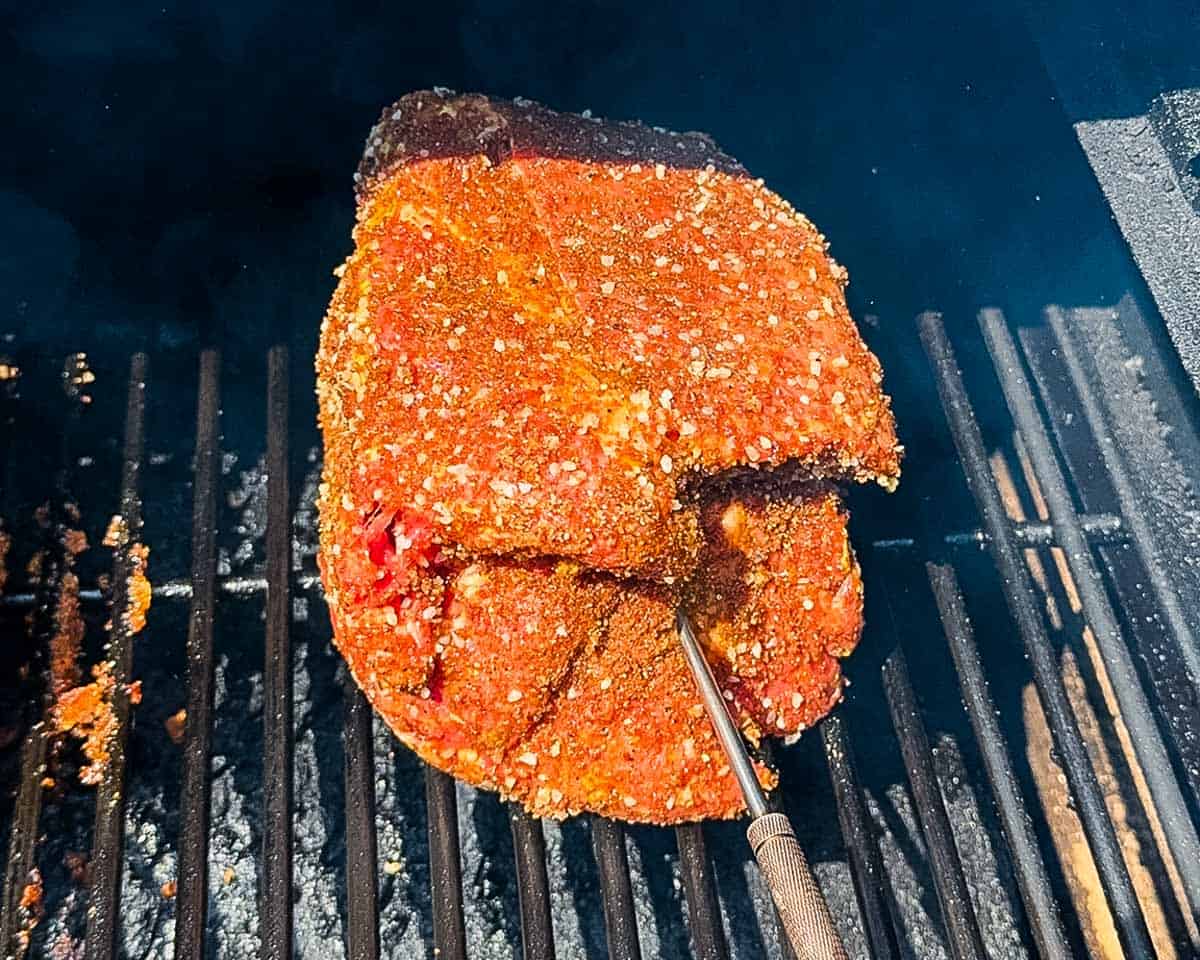 Seasoned beef roast on pellet grill grates with temperature probe inserted.