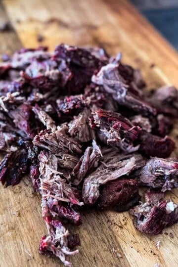 Smoked pulled beef made from chuck roast, shredded into juicy pieces with a dark bark on a wooden cutting board.