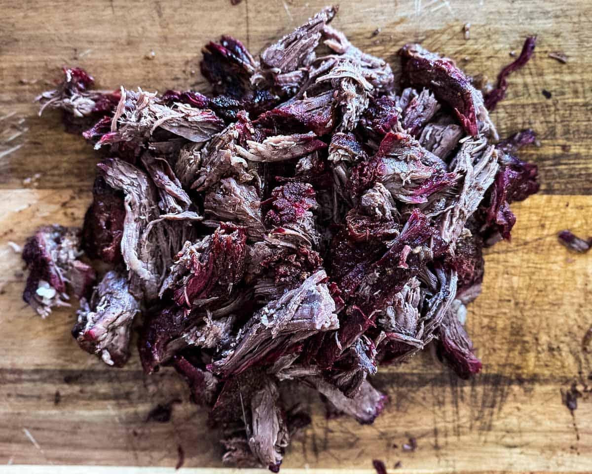Shredded smoked chuck roast pulled into tender pieces on wooden cutting board.