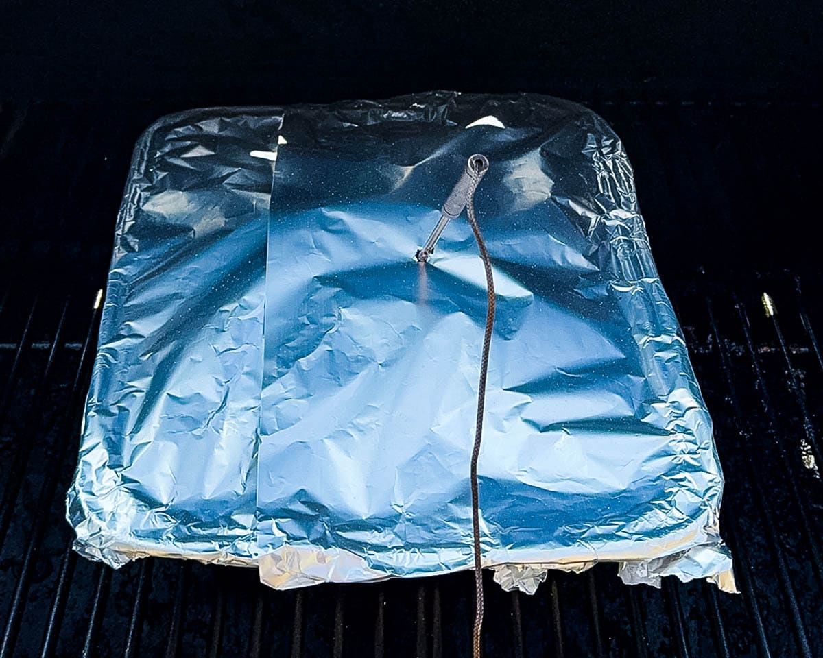 Foil-covered pan with smoked chuck roast on pellet grill with temperature probe inserted.