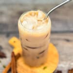 Iced Starbucks chai tea latte copycat in a glass with ice and creamy milk on a wooden board.