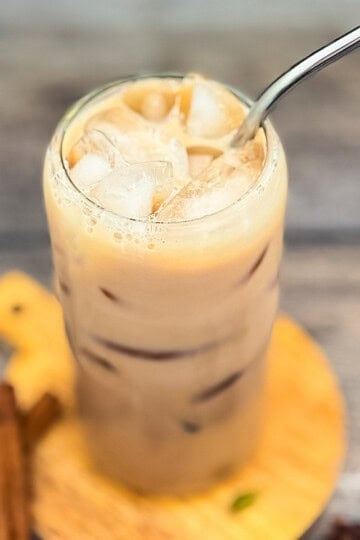 Iced Starbucks chai tea latte copycat in a glass with ice and creamy milk on a wooden board.