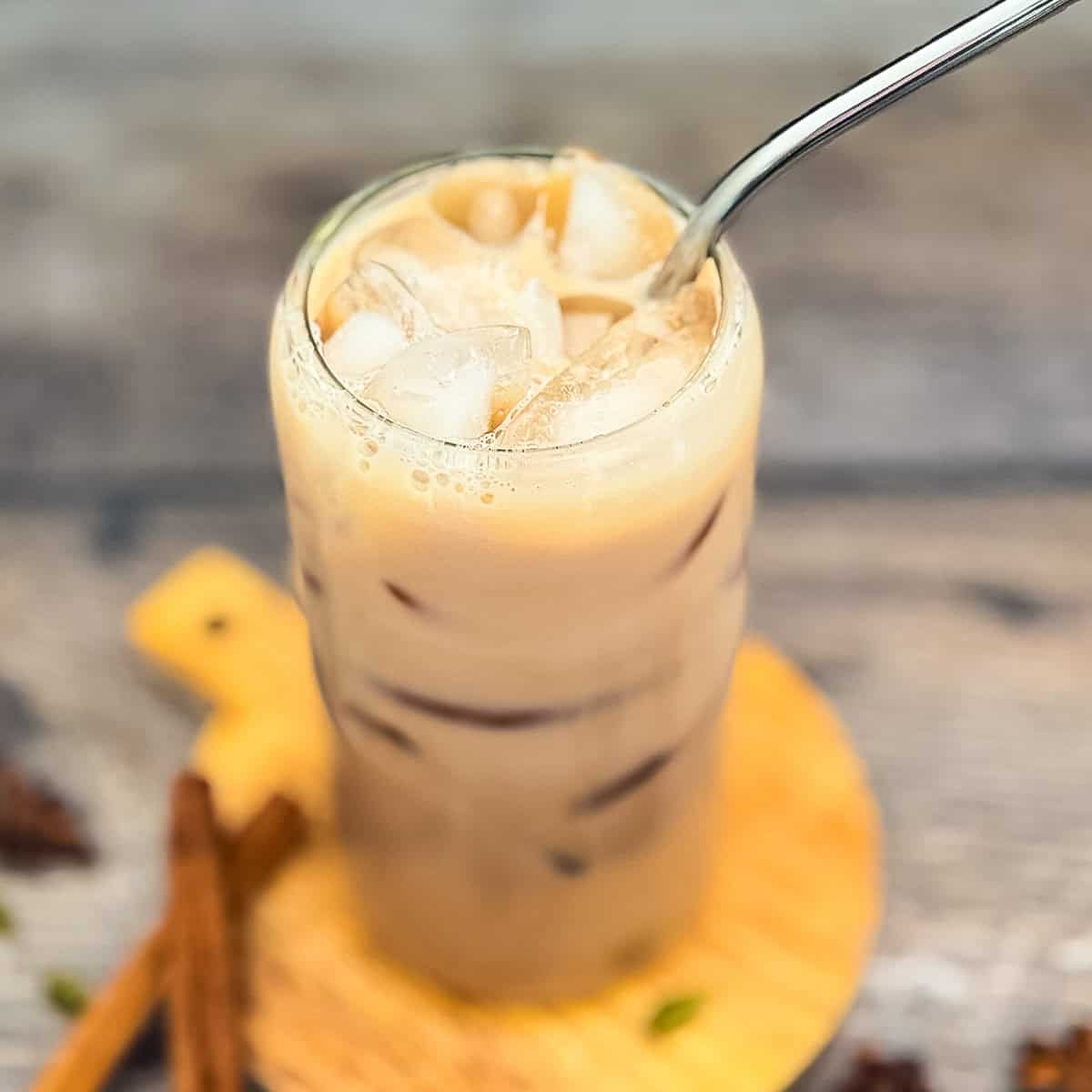 Iced Starbucks chai tea latte copycat in a glass with ice and creamy milk on a wooden board.