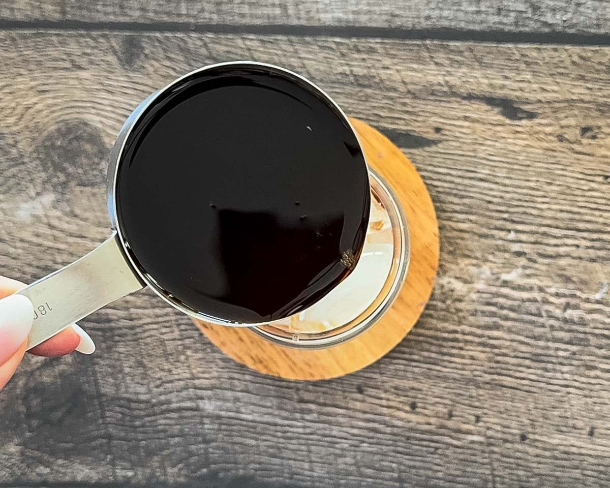 Pouring chai tea concentrate over ice in glass.